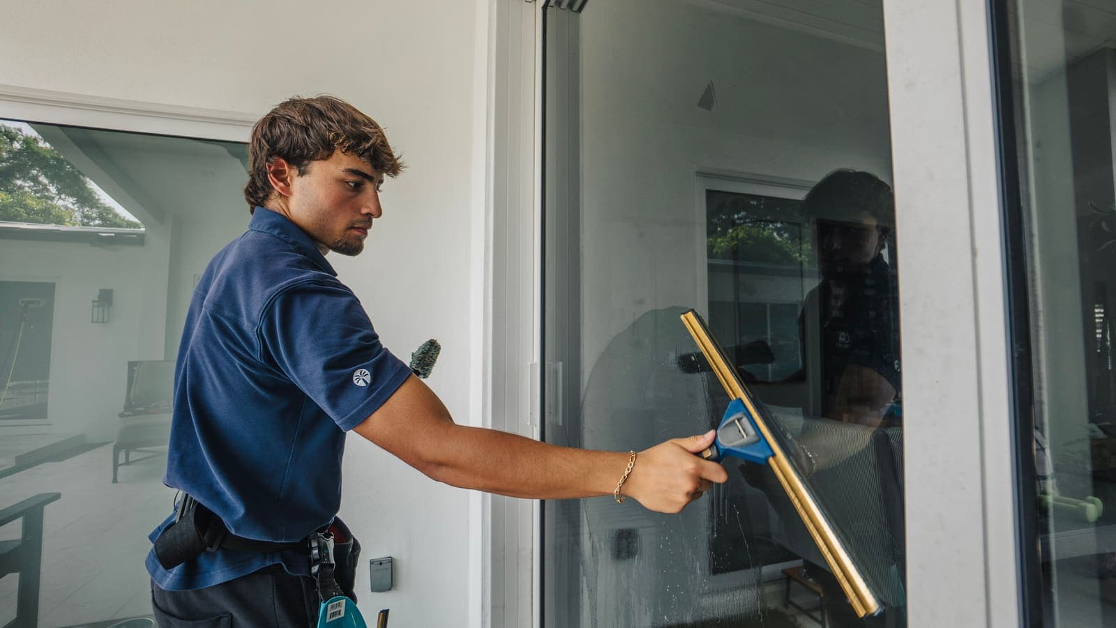 Coast technician pulling a brass squeegee across sliding glass door panes at a Miami home