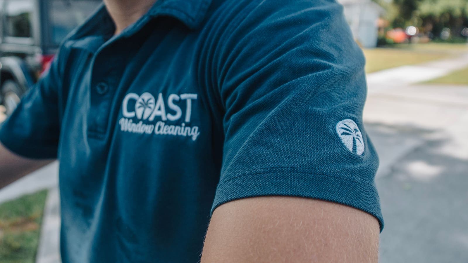 COAST Window Cleaning chest embroidery and palm sleeve patch on a technician's navy polo