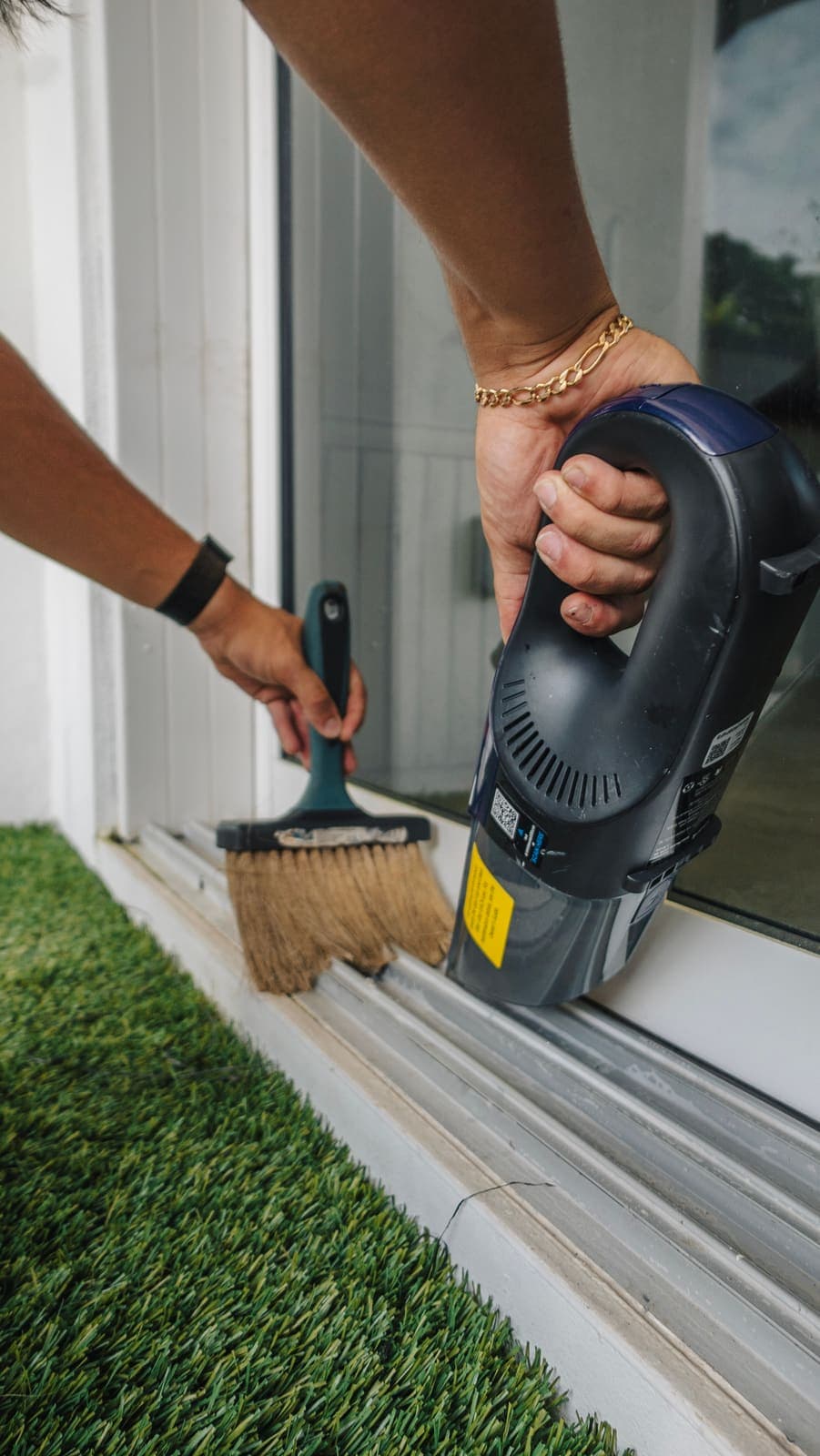 Track brush and handheld vacuum clearing a sliding-door track together